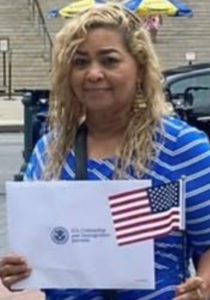 Contributing writer Sobeida Valle celebrates her citizenship. She smiles at the camera, wearing a blue-and-white-striped shirt and carrying official papers and an American flag