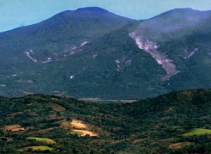 photograph of wooded mountains showing evidence of earthquake damage in a big swath of bare earth and falling rock
