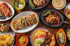 photo shows many dishes of Mexican food, including tacos, stuffed peppers, and rice and beans