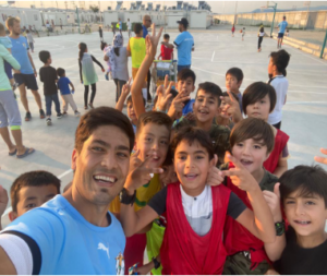 photo shows a smiling man in a jersey taking a selfie with a group of grinning children