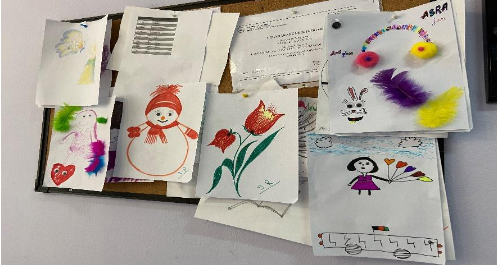 photograph shows many colorful works of children's art pinned to a bulletin board
