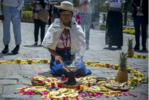 photograph of a woman in traditional costume kneeling in a city square and making an offering of fruit