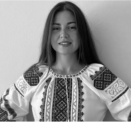 black-and-white photograph shows the author standing confidently, smiling at the camera and facing forward with her hands on her hips, wearing vyshyvanka -- an elaborately embroidered white blouse
