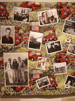 a quilted wall hanging with a World War theme: black and white photographs featuring men and women in uniform appear over a background featuring American flags and vintage trucks