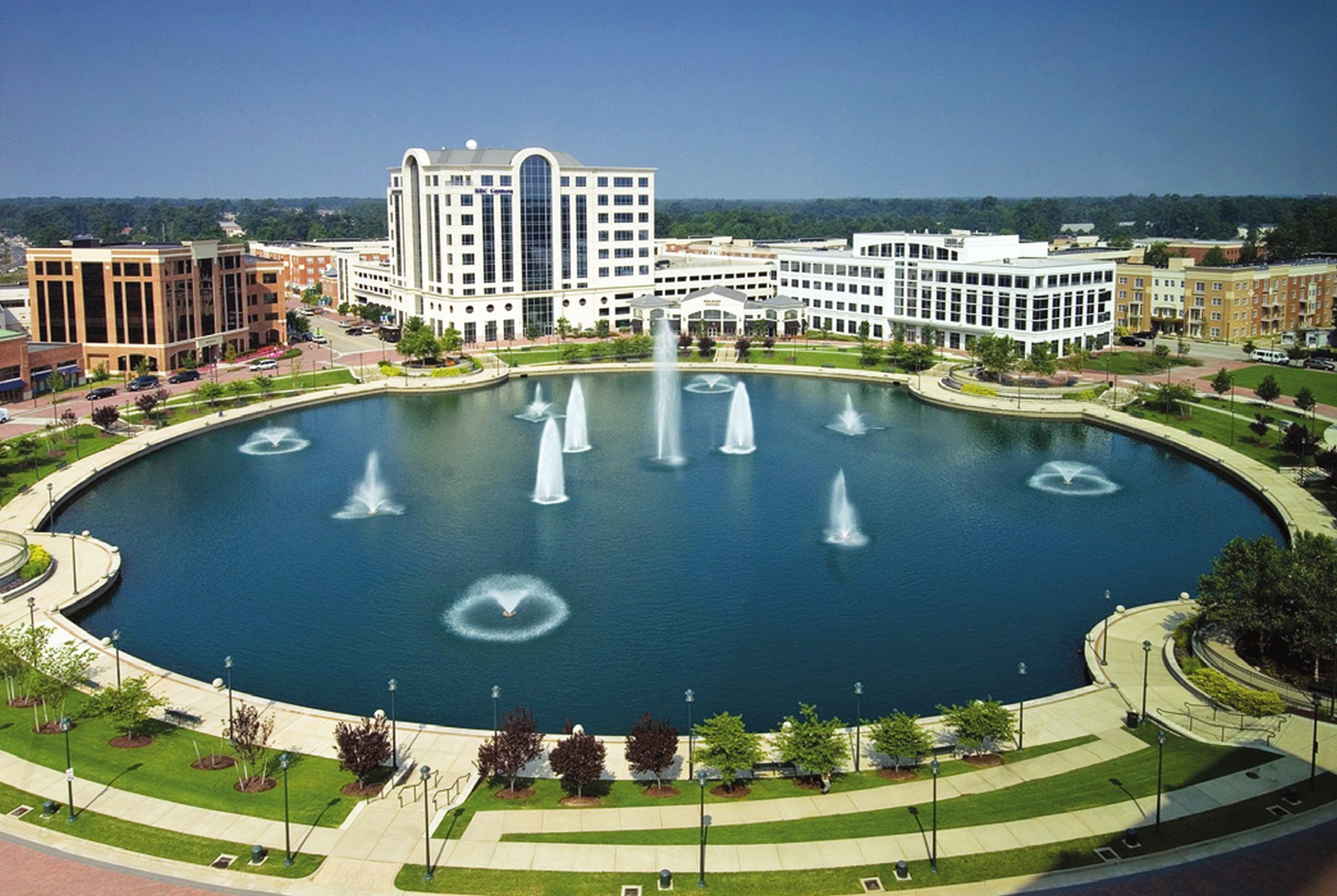 photograph of a luxurious Newport News hotel or conference center, with tall buildings rising behind an artificial lake sporting fountains
