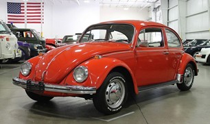 photo of shiny red Beetle parked in a showroom with an American flag hanging behind it