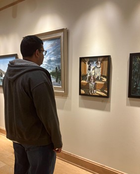 photo of the author, standing in silhouette as he views the framed painting of three dogs