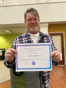 a smiling, bearded middle-aged man holds up a certificate